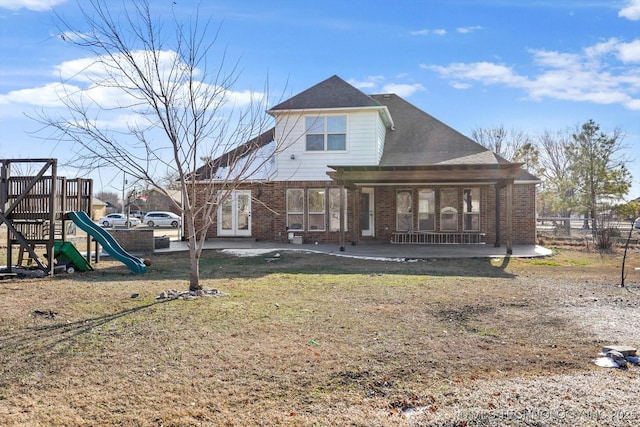 rear view of property featuring a shingled roof, a lawn, a patio, a playground, and brick siding