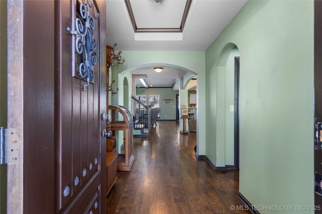 foyer entrance with arched walkways, dark wood finished floors, stairway, and baseboards