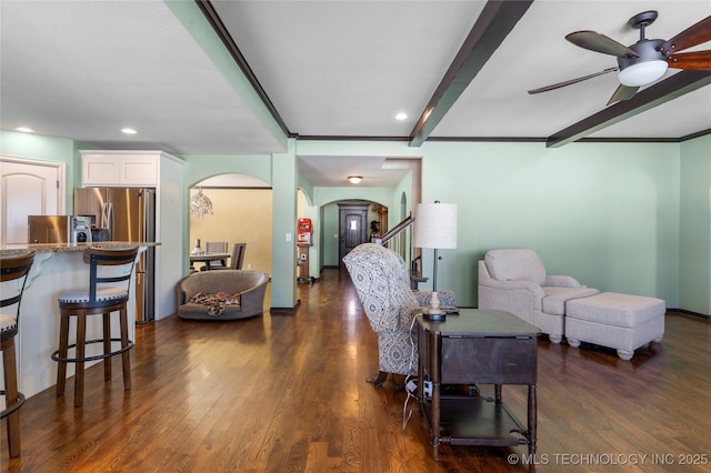 living room featuring arched walkways, ceiling fan, stairway, beamed ceiling, and dark wood finished floors