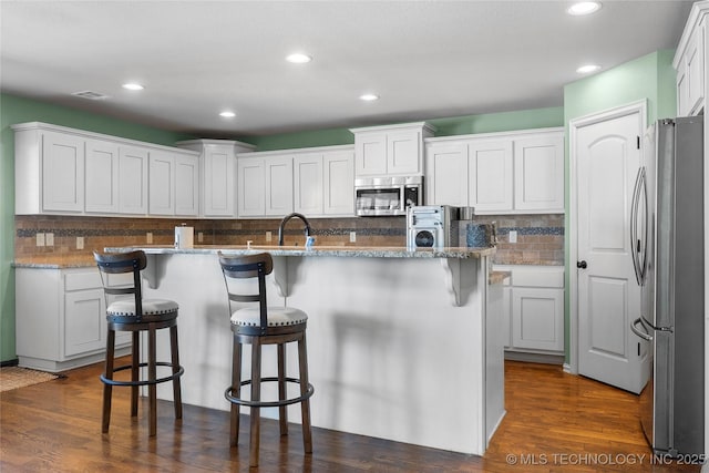 kitchen with a kitchen breakfast bar, stainless steel appliances, a center island with sink, and white cabinetry