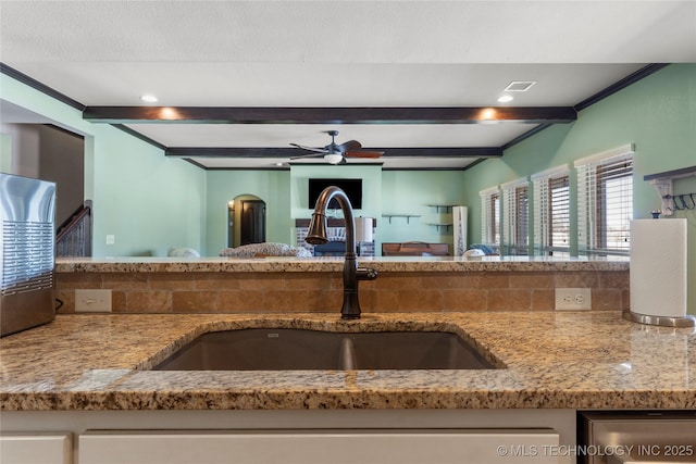 kitchen with ceiling fan, beamed ceiling, light stone countertops, white cabinetry, and a sink