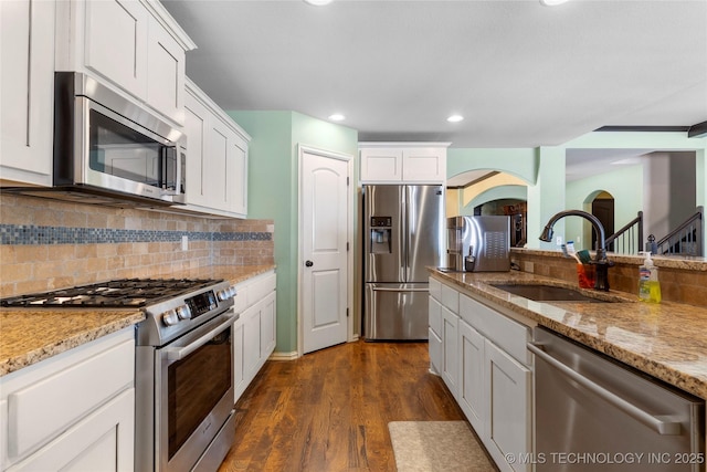 kitchen featuring stainless steel appliances, a sink, white cabinets, backsplash, and light stone countertops