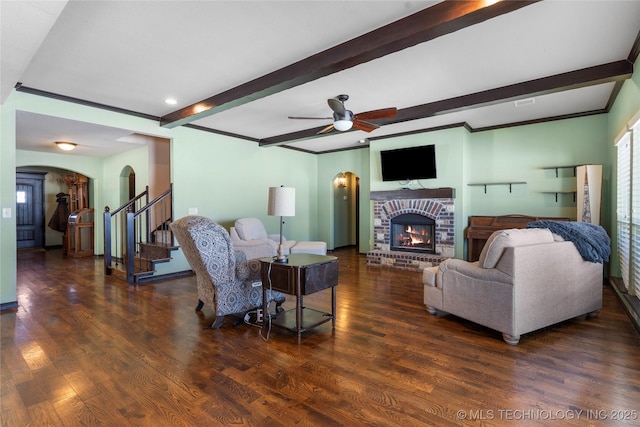 living room with arched walkways, stairway, dark wood-style flooring, a brick fireplace, and beam ceiling