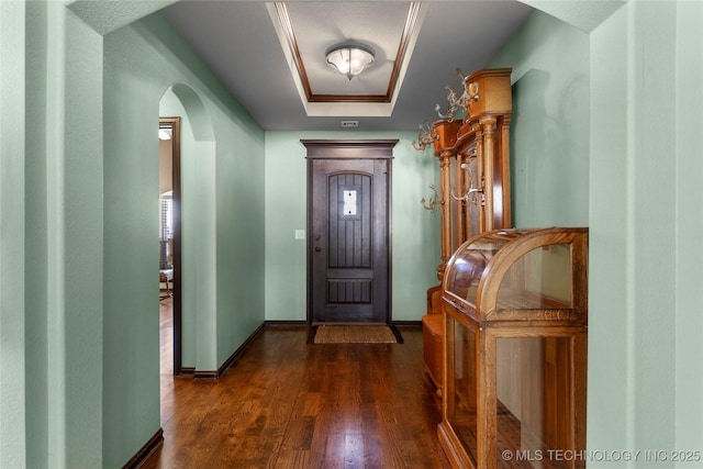 foyer featuring dark wood-type flooring, arched walkways, baseboards, and a tray ceiling