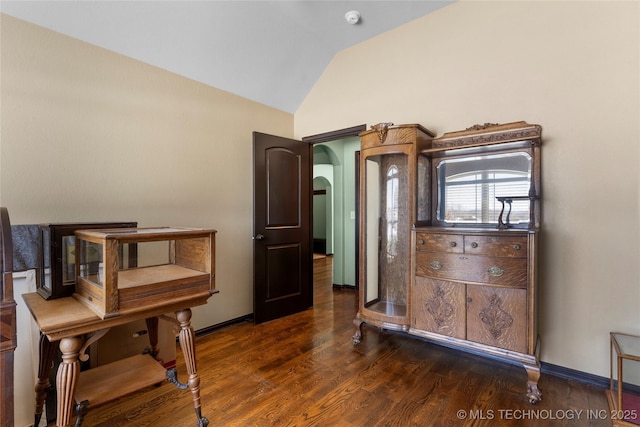 bedroom featuring lofted ceiling, dark wood-style flooring, arched walkways, and baseboards