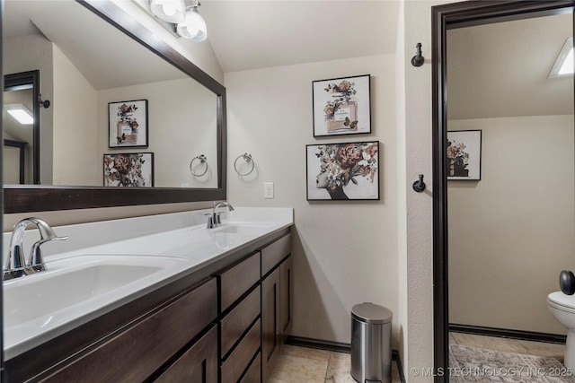 full bath featuring baseboards, a sink, toilet, and double vanity