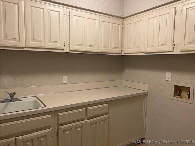 washroom featuring a textured wall, washer hookup, a sink, and cabinet space