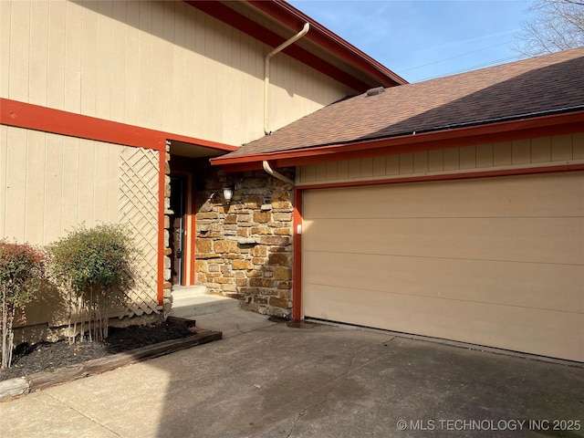 doorway to property featuring an attached garage, stone siding, and roof with shingles