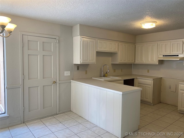 kitchen featuring light tile patterned floors, a peninsula, light countertops, under cabinet range hood, and a sink