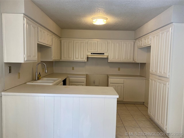 kitchen featuring light tile patterned floors, under cabinet range hood, a peninsula, a sink, and light countertops