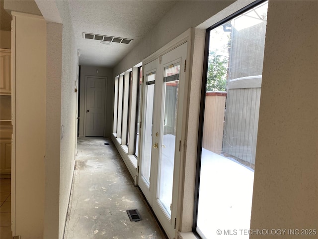 corridor featuring concrete flooring, visible vents, a textured wall, and a textured ceiling