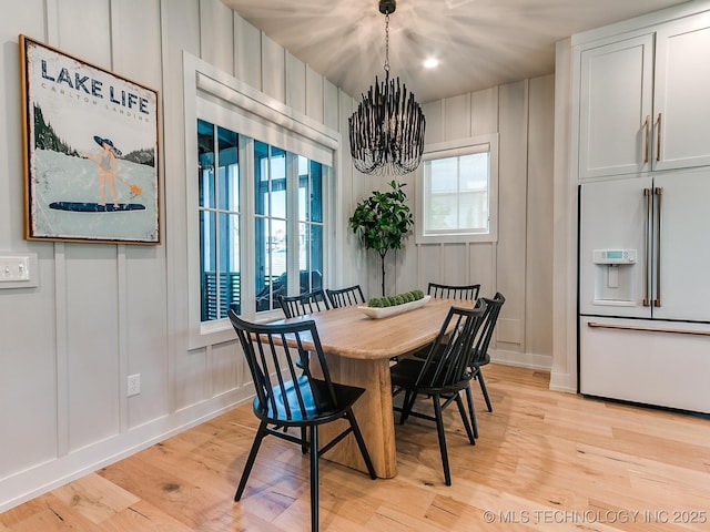 dining space featuring a notable chandelier, light wood-style floors, and a decorative wall