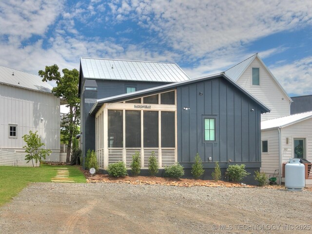 back of property with a sunroom, a lawn, metal roof, and board and batten siding