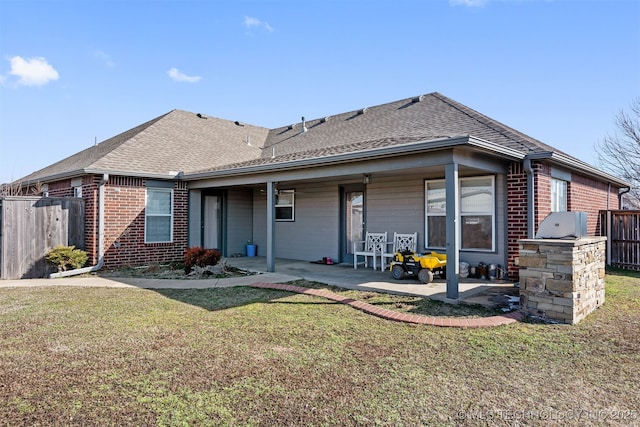 rear view of house with brick siding, a yard, a patio, roof with shingles, and fence