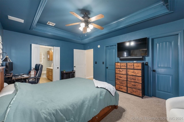 bedroom featuring crown molding, a raised ceiling, light colored carpet, visible vents, and ensuite bath