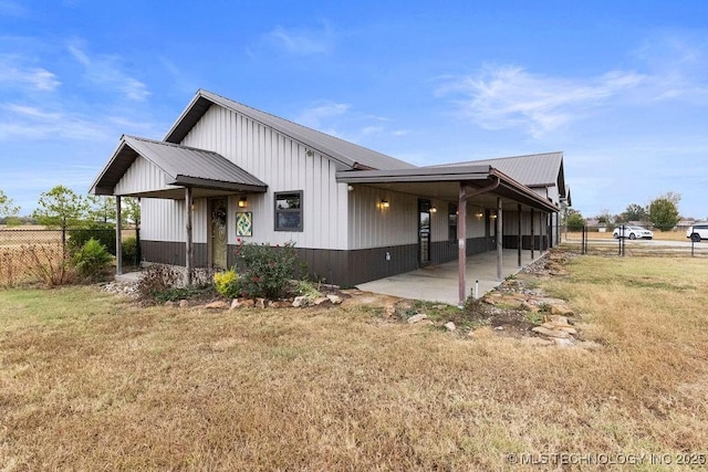 view of side of property with a patio area, fence, metal roof, and a yard