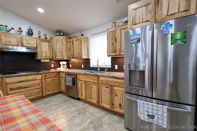 kitchen featuring tasteful backsplash, dark stone counters, appliances with stainless steel finishes, under cabinet range hood, and a sink