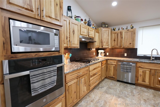 kitchen featuring tasteful backsplash, appliances with stainless steel finishes, stone countertops, a sink, and under cabinet range hood