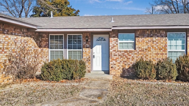 doorway to property with brick siding and roof with shingles