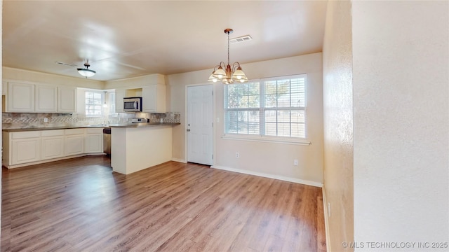 kitchen with pendant lighting, tasteful backsplash, light countertops, stainless steel microwave, and white cabinets