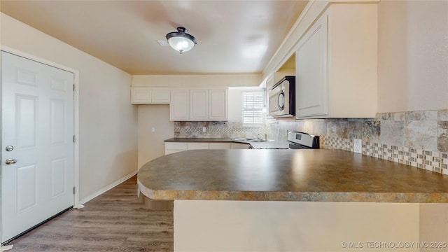 kitchen with light wood-style flooring, stainless steel appliances, a peninsula, white cabinetry, and decorative backsplash