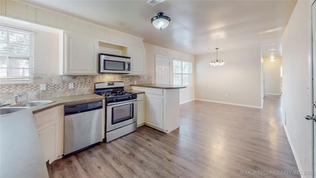 kitchen with a peninsula, white cabinetry, appliances with stainless steel finishes, backsplash, and decorative light fixtures