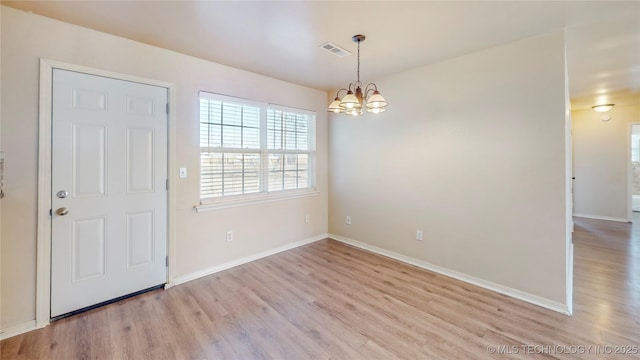 empty room featuring baseboards, light wood-type flooring, visible vents, and an inviting chandelier