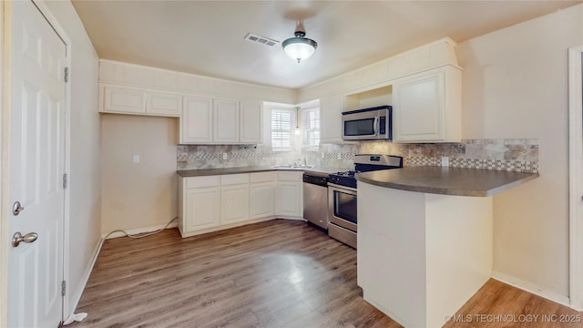 kitchen featuring white cabinets, dark countertops, appliances with stainless steel finishes, light wood-style floors, and backsplash