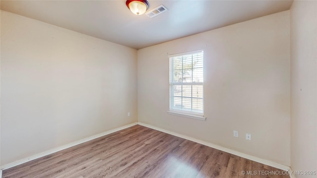 unfurnished room featuring wood finished floors, visible vents, and baseboards