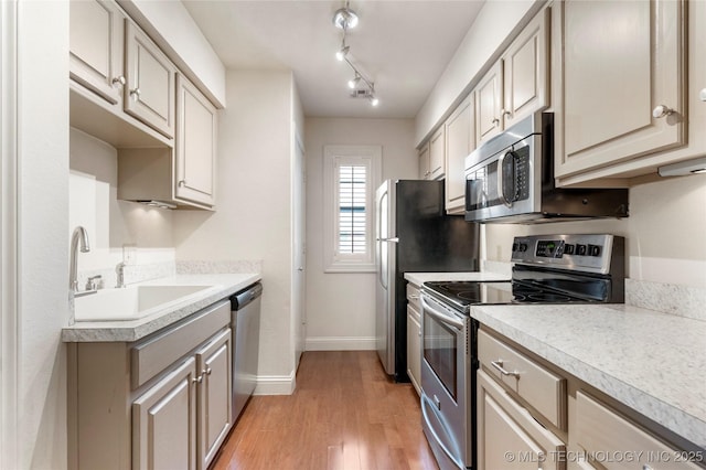 kitchen with light wood-style flooring, stainless steel appliances, a sink, baseboards, and light countertops