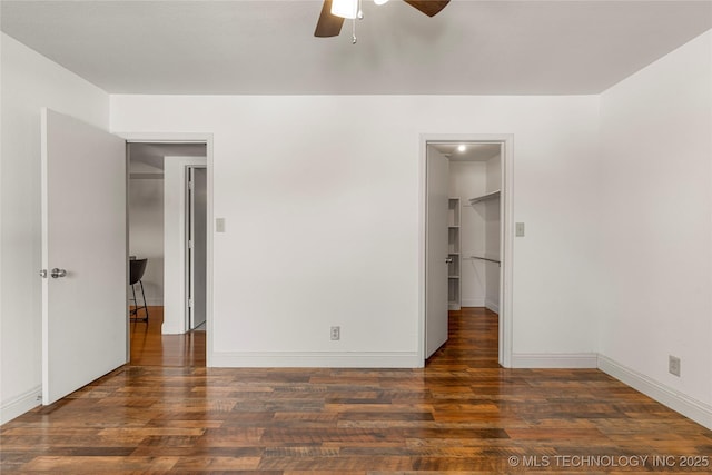 unfurnished bedroom with a ceiling fan, a spacious closet, baseboards, and dark wood-type flooring