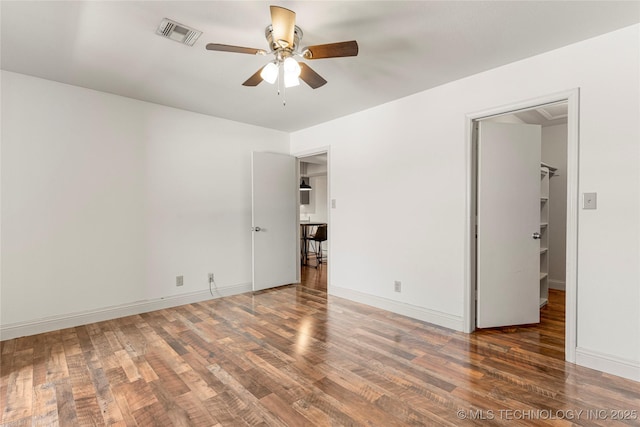 unfurnished bedroom with baseboards, a spacious closet, visible vents, and dark wood finished floors