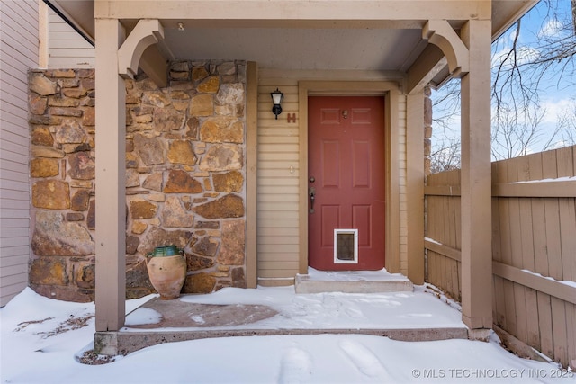 snow covered property entrance with stone siding and fence