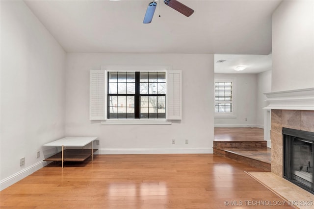 unfurnished living room featuring baseboards, ceiling fan, a tiled fireplace, and light wood-style floors