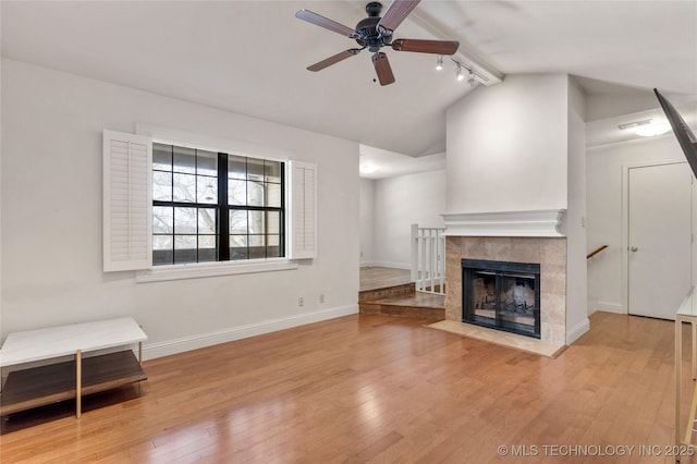 unfurnished living room featuring baseboards, a ceiling fan, vaulted ceiling, light wood-type flooring, and a fireplace