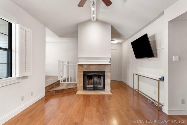 unfurnished living room with ceiling fan, a fireplace, wood finished floors, baseboards, and vaulted ceiling