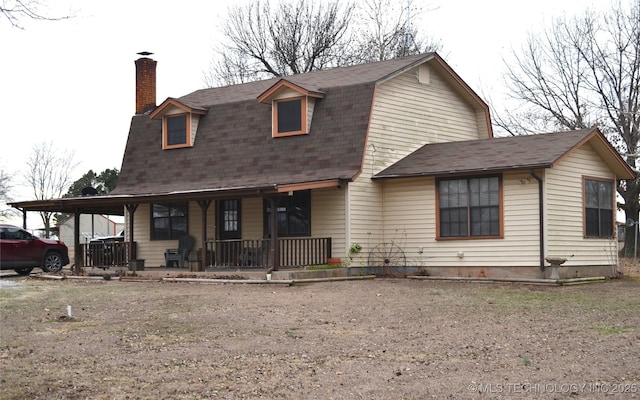 dutch colonial with covered porch, roof with shingles, a chimney, and a gambrel roof