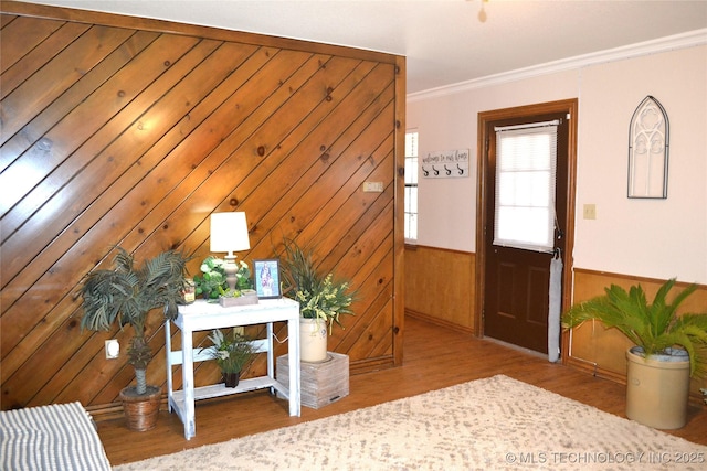 foyer entrance featuring wainscoting, crown molding, wooden walls, and wood finished floors