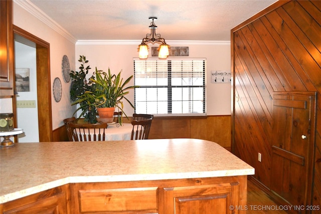 kitchen featuring wooden walls, ornamental molding, brown cabinets, light countertops, and pendant lighting