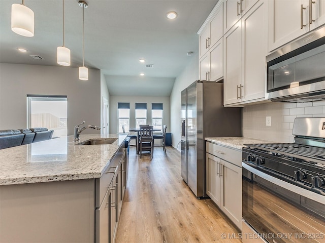 kitchen with white cabinets, appliances with stainless steel finishes, a kitchen island with sink, pendant lighting, and a sink