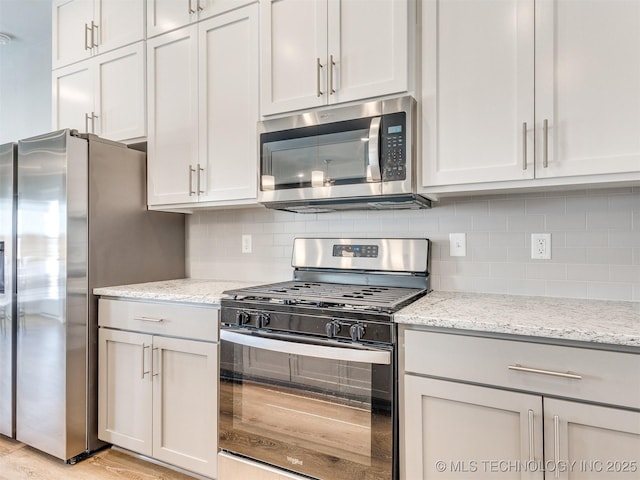 kitchen with stainless steel appliances, white cabinetry, backsplash, and light stone counters