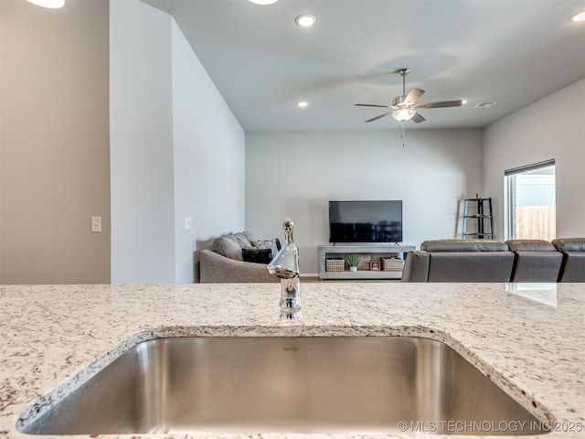 kitchen with light stone counters, recessed lighting, a sink, a ceiling fan, and open floor plan