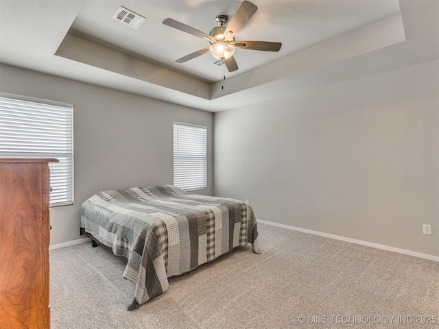 bedroom featuring a tray ceiling, visible vents, and multiple windows