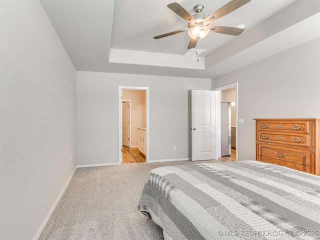 bedroom with light carpet, baseboards, a tray ceiling, and ensuite bathroom