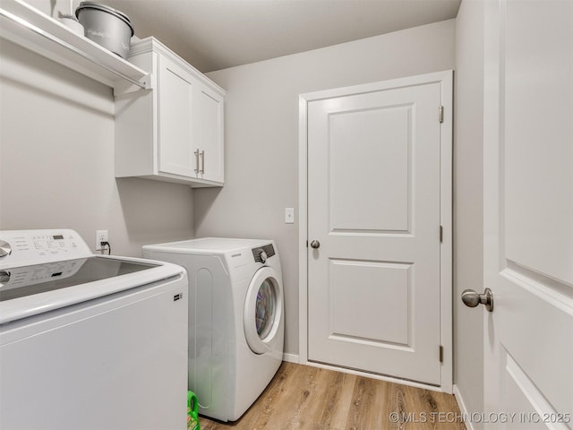 washroom featuring light wood finished floors, washer and clothes dryer, cabinet space, and baseboards