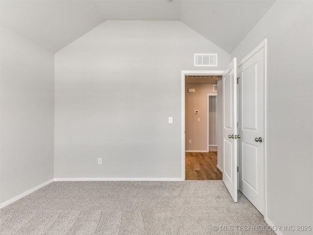 interior space featuring light carpet, vaulted ceiling, visible vents, and baseboards