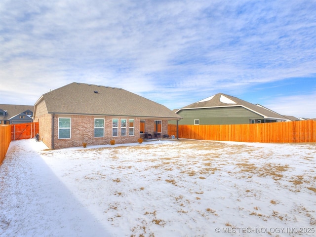 snow covered rear of property featuring brick siding, a shingled roof, and a fenced backyard