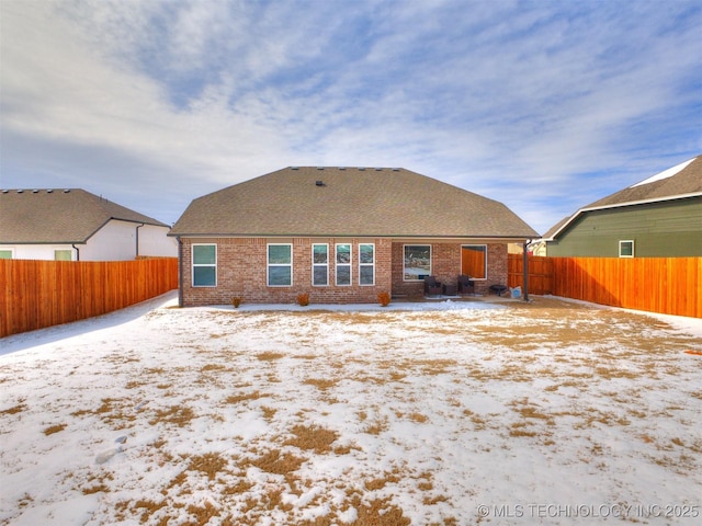 snow covered property with a fenced backyard, roof with shingles, and brick siding