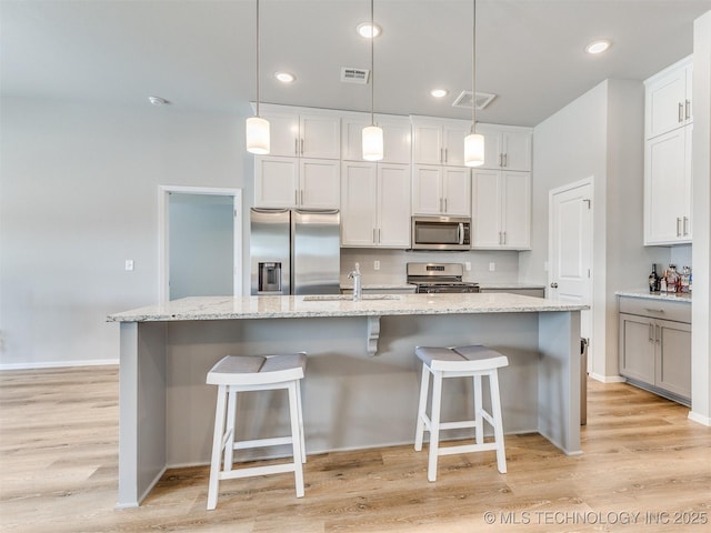 kitchen with an island with sink, a breakfast bar area, stainless steel appliances, and decorative light fixtures