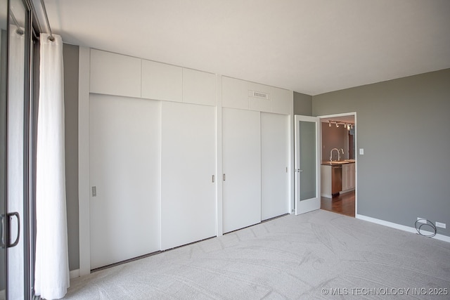 unfurnished bedroom featuring two closets, baseboards, a sink, and light colored carpet